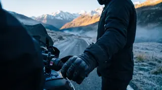 Heated motorcycle gloves on the handlebar on a frosty alpine road at sunrise
